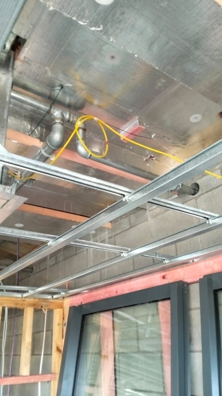 Foil-faced rigid insulation board fixed to a soffit above steel framing and services